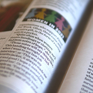 A close-up of an open magazine page featuring an article titled “WOMEN IN 2014” with blurred text and a colorful banner of silhouettes at the top of the page.