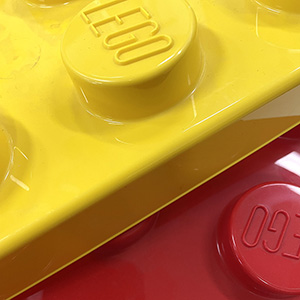 Close-up of large yellow and red LEGO bricks, with the LEGO logo visible on the raised circular studs. The bright colors and shiny surfaces are clearly shown.