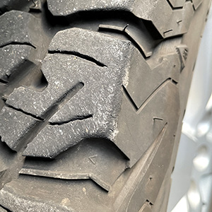 Close-up of a rugged vehicle tire with deep, angular treads, showing detailed patterns and some dirt on the rubber surface.