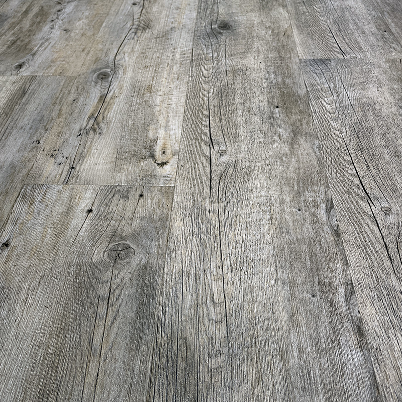 Close-up view of a light gray wooden floor with visible grain patterns and knots, showing a rustic and textured surface.