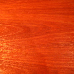 A close-up of a smooth wooden surface with a reddish-brown finish, visible natural grain patterns, and a subtle sheen.