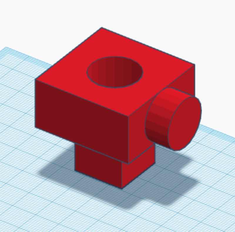 A 3D model of a red geometric object featuring a large cube with a circular hole on top, a cylinder protruding from one side, and a smaller rectangular base, displayed on a grid workspace.
