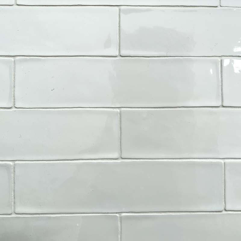 Close-up of a white subway tile wall with a glossy finish and visible grout lines, arranged in a horizontal brick pattern.