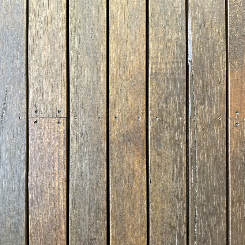 Close-up view of wooden floorboards arranged vertically, with visible wood grain, natural brown tones, and several small screws attaching the planks together. The surface appears smooth and well-maintained.