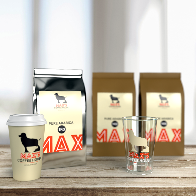 A coffee cup, glass, and three coffee bags with MAXS COFFEE HOUSE and a dog logo are displayed on a wooden surface, with a blurred background. The bags are labeled Pure Arabica.