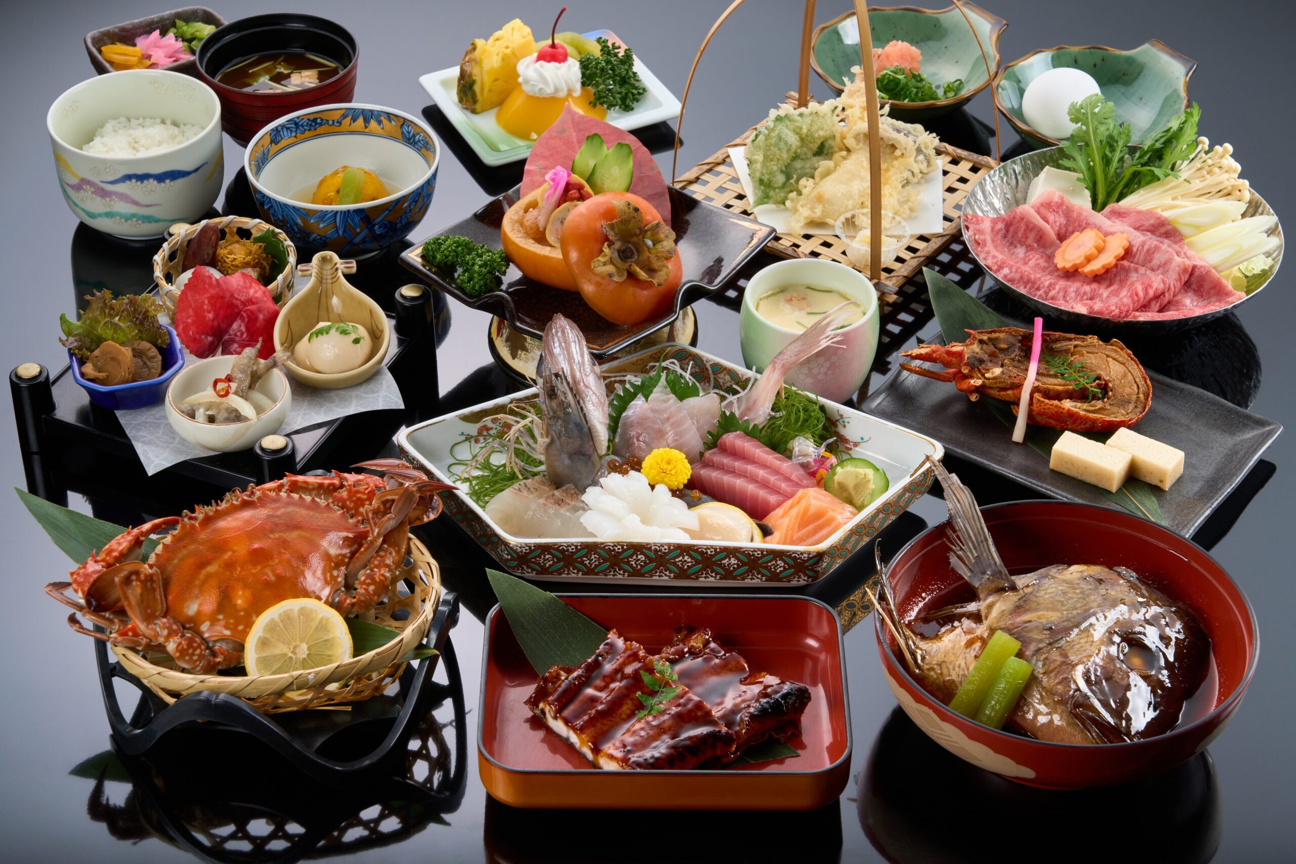 A traditional Japanese kaiseki meal featuring assorted seafood, sashimi, grilled meats, rice, soup, vegetables, and colorful side dishes, all beautifully arranged in various bowls and plates on a glossy black surface.