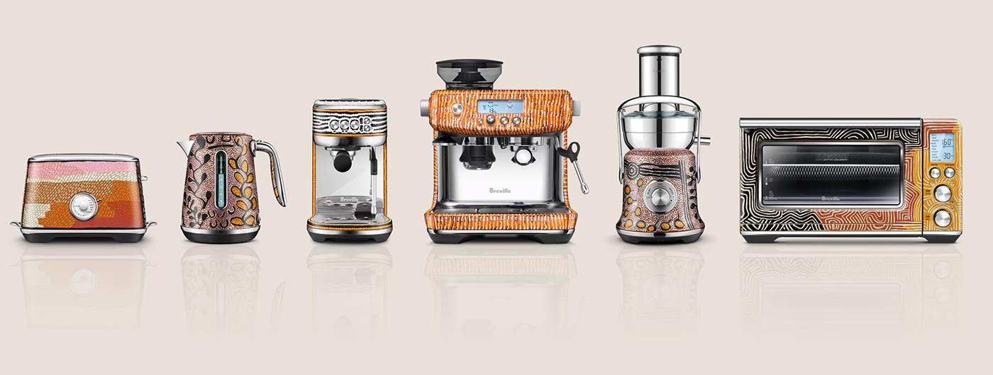 Six kitchen appliances, including a toaster, kettle, coffee machine, blender, juicer, and toaster oven, are decorated with colorful, patterned Aboriginal-inspired designs, arranged in a row against a neutral background.
