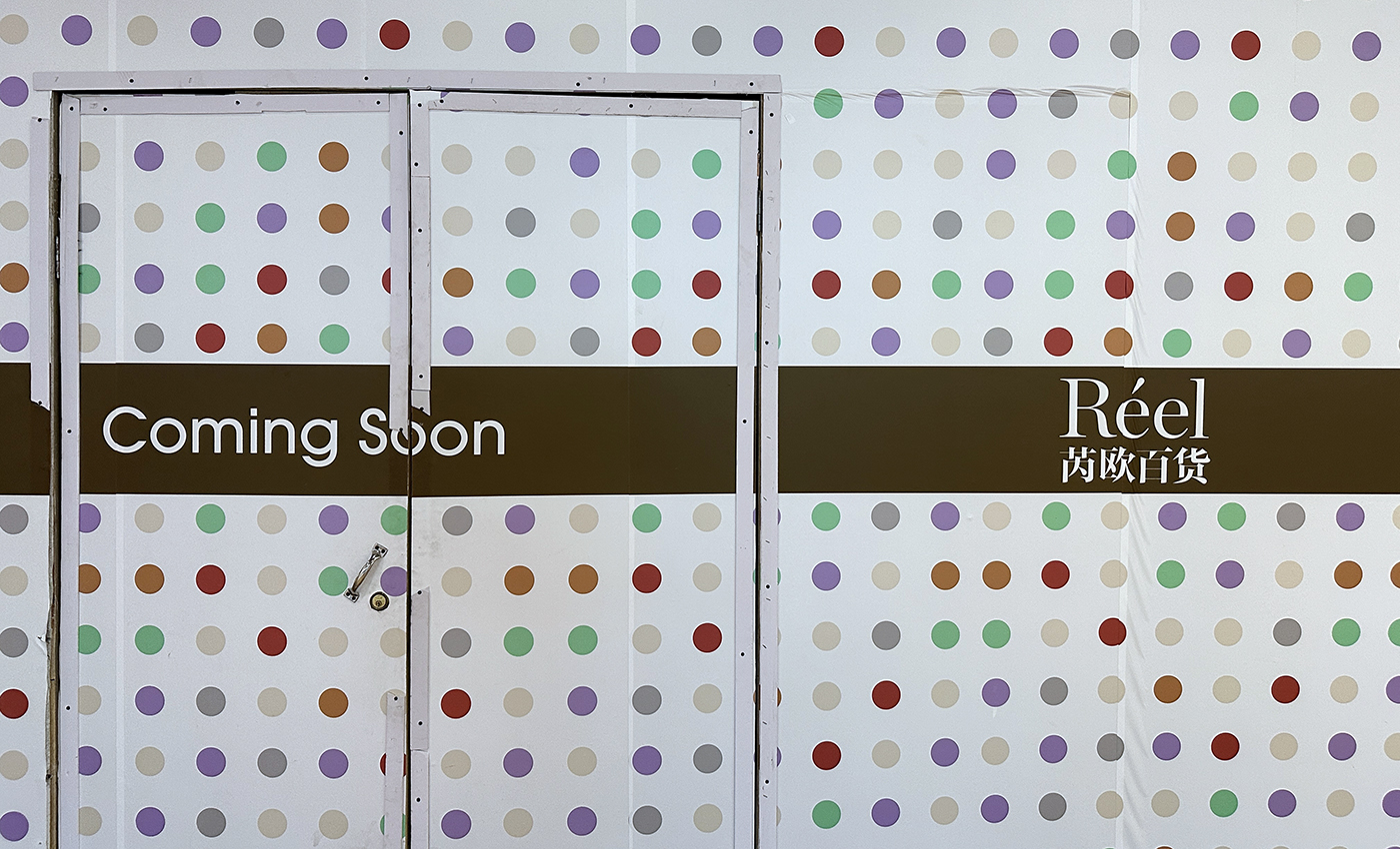 A wall with a polka dot pattern in various colors features the text Coming Soon and Réel with Chinese characters, covering a closed door.