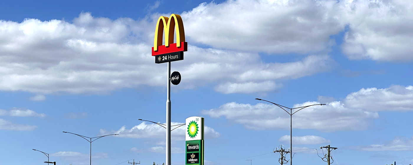 A tall McDonald’s sign and a BP gas station sign stand against a blue sky with scattered clouds. Streetlights and power lines are visible in the background.